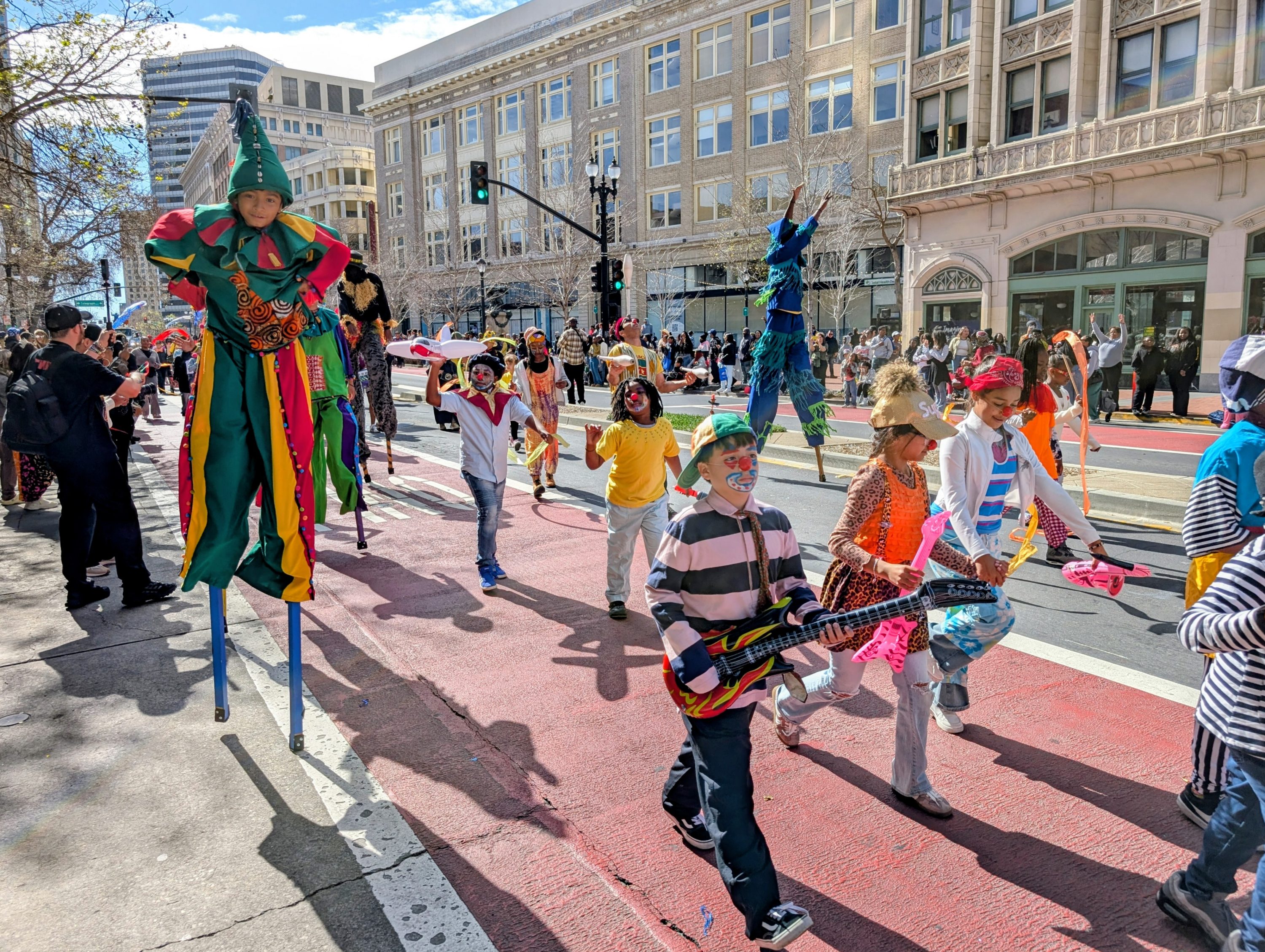 a group of children in colorful costumes carrying toy instruments parade in the Black Joy Parade as a clown band