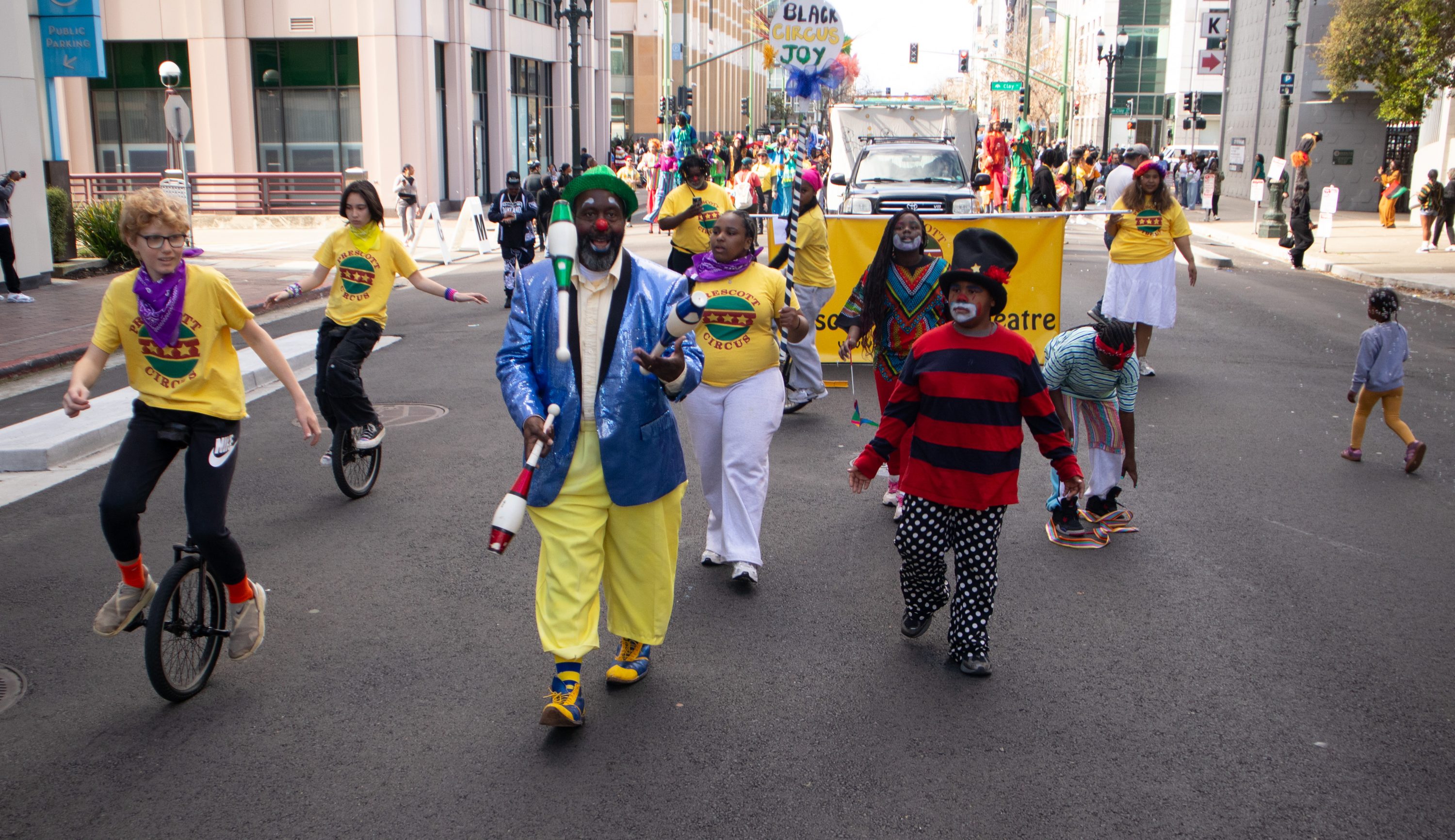 Jamarr Woodruff, Prescott Circus teaching artist, is wearing a shiny blue jacket and yellow pants is juggling as he leads the parade along side students in costume riding unicycles and walking.